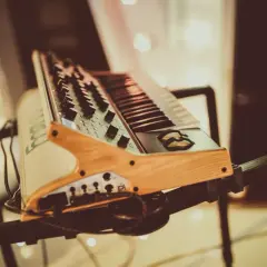 Keyboard muzyczny na czarnym statywie, z drewnianymi elementami.
